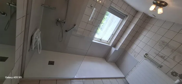 Na: brede inloopdouche bij het raam met douchezitje, steunbeugel en glazen wand