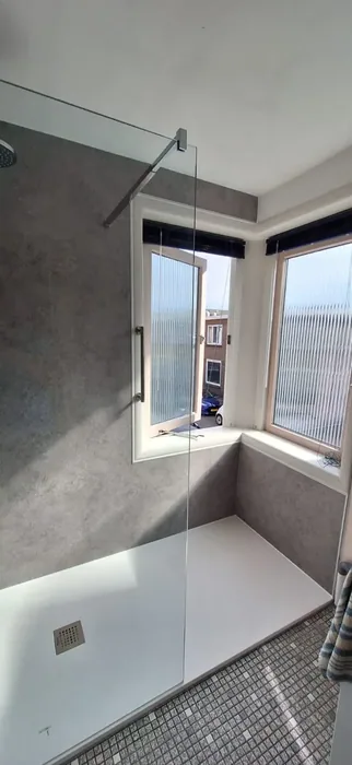 Ruime inloopdouche bij een erkerraam met grijze betonlook wandpanelen en glazen wand