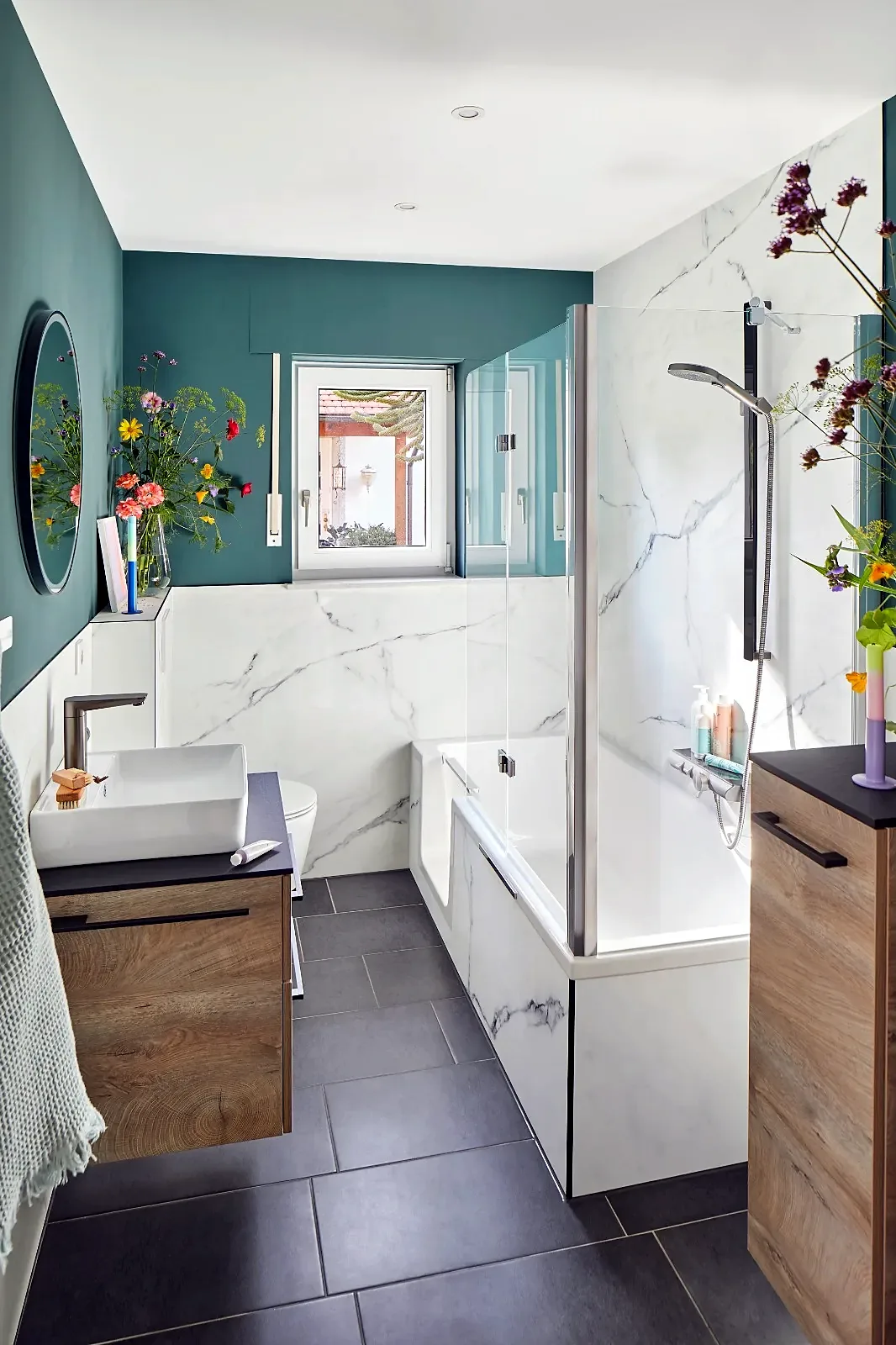 Badkamer met groene wand, marmerlook tegels, houten meubel en bad