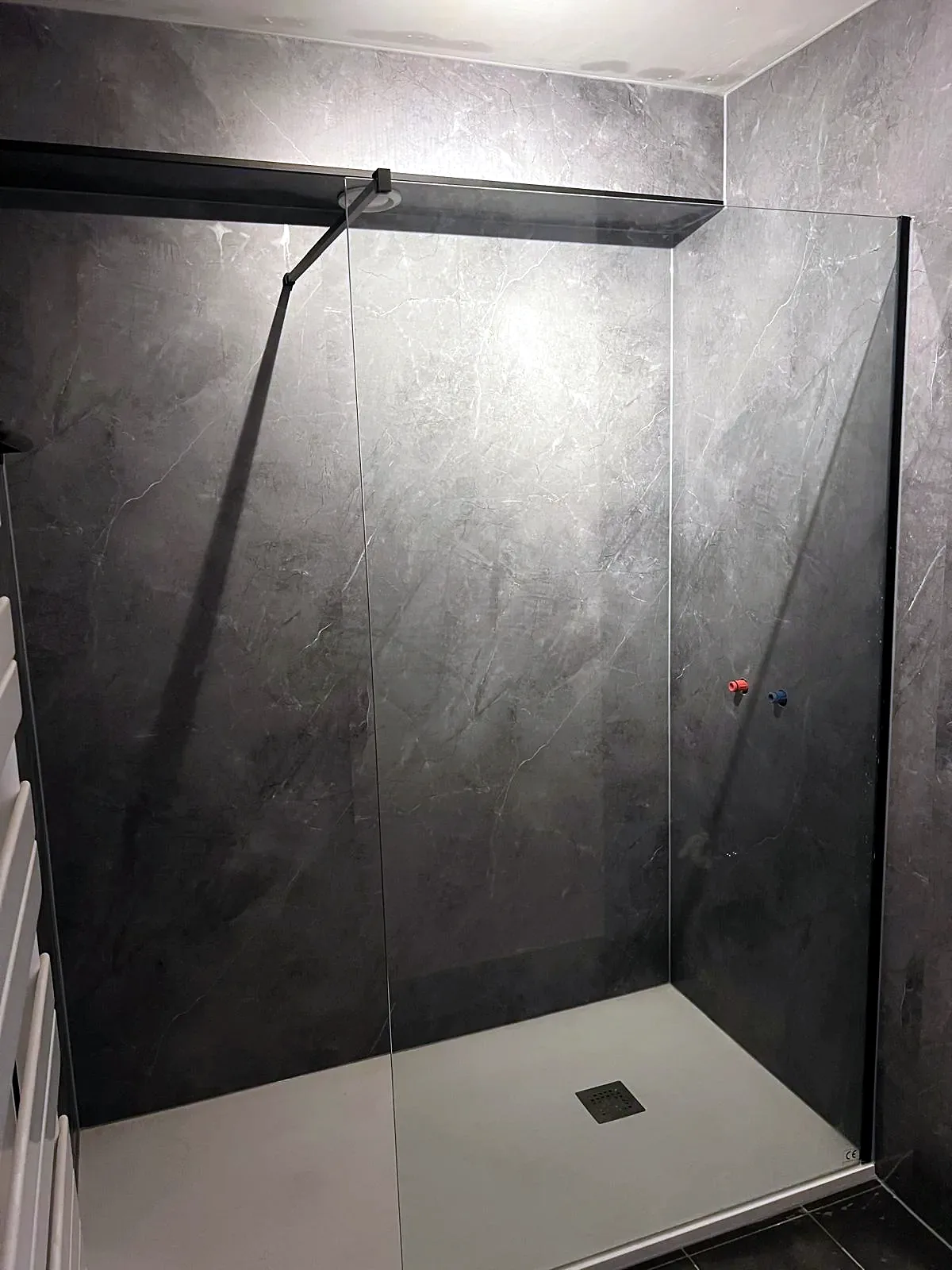 Inloopdouche met witte douchebak, glazen wand met zwarte profielen en donkergrijze panelen