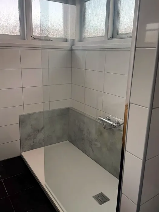 Na: lage douchebak met grijze wandpanelen en glazen wand op de plek van het bad